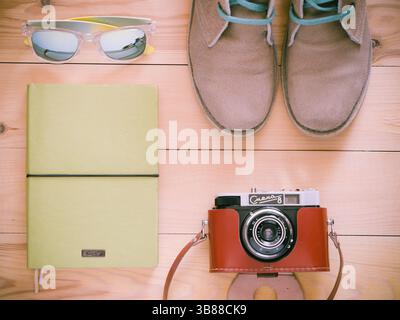 Set of travel and resort stuff. Old 35 mm camera, note book, sunglasses and desert boots on wooden table. Top view, flat lay. Toned image Stock Photo