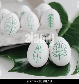 Drawings eggs with tropical leaves. Tropical easter eggs concept. Green monstera plants and tropical palm leaves painted on egg shell. Easter holiday Stock Photo