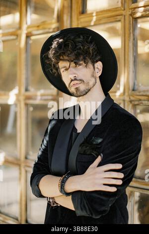Young man in a black hat stands with his arms crossed against the background of a wooden window. Stock Photo