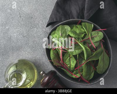 Fresh salad of green chard leaves or mangold on gray stone background. Flat lay or top view fresh baby beet leaves in craft ceramic bowl Stock Photo