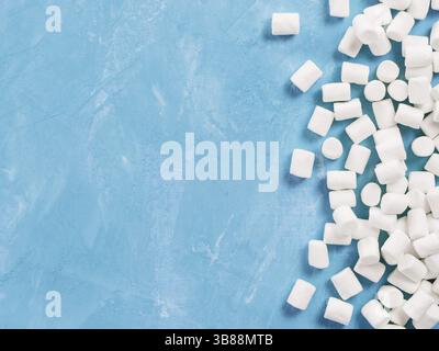 Marshmallows on blue background with copyspace. Flat lay or top view. Background or texture of colorful mini marshmallows. Winter food background conc Stock Photo