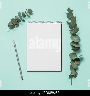 Blank notebook, pencil and eucalyptus on blue background. Empty notebook paper and eucalyptus branch on pastel blue background with copy space for tex Stock Photo