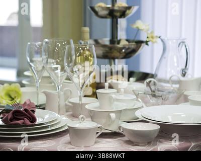 Set of new dishes on table with tablecloth. Stack of white plates and wine glasses on restaurant table. Shallow DOF Stock Photo