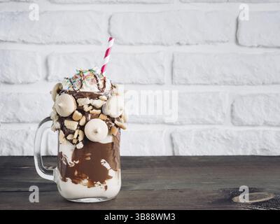 Close up view of freakshake in mason jar on brown table. Freaked milkshake with chocolate, biscuit cookies and sugar sprinkling. Copy space. Trendy fo Stock Photo