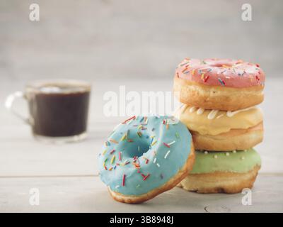 Donuts and coffee on gray wooden table with copy space. Colorful donuts and coffee cup on grey wooden background with copyspace. Glazed doughnuts in s Stock Photo