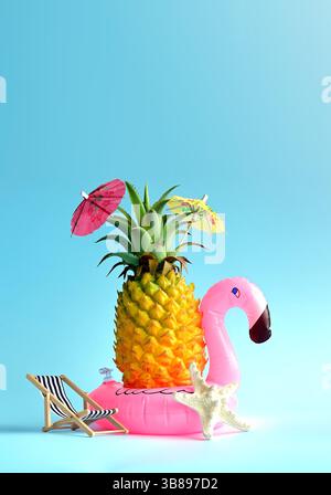 Summer concept, pineapple on blue background near a sun lounger, pink flamingo and umbrella. Stock Photo