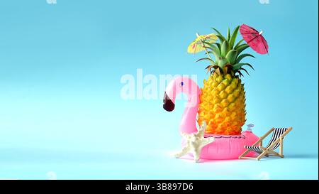 Summer concept, pineapple on blue background near a sun lounger, pink flamingo and umbrella. Stock Photo