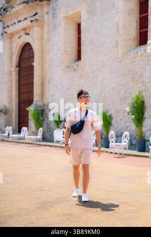 Latino man dressed in casual beige outfit walks happily past historic stone wall on a sunny day in Cartagena, Colombia. Stock Photo