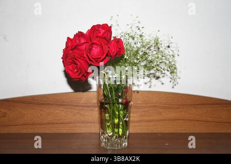 The red roses are in the glass vase on the wooden shelf. Stock Photo