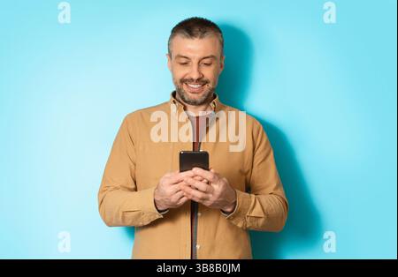 Cheerful Man Using Mobile Application On Cellphone Over Blue Background Stock Photo