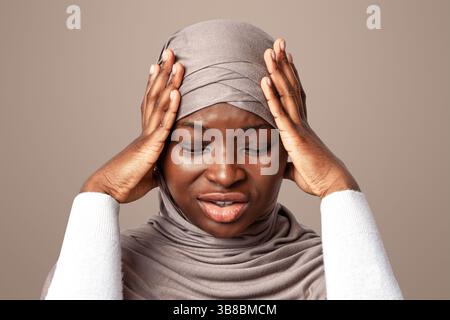 Upset Black Islamic Lady In Hijab Having Strong Headache, Touching Temples Stock Photo