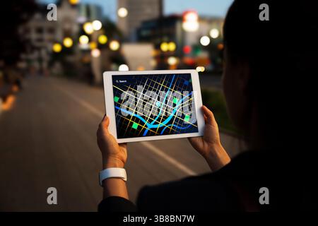 Woman using  tablet with a digital city map on street at night Stock Photo