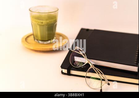 Close-up of a stack of books and a freshly made matcha latte in a ceramic cup, creating a warm and calming reading atmosphere. Stock Photo