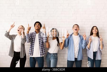 Teen friends pointing up on free space over white wall Stock Photo