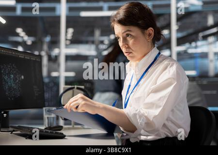 Data center admin monitoring system performance using PC, looking over maintenance paperwork. Server farm worker reading documentation files to implement optimizations Stock Photo