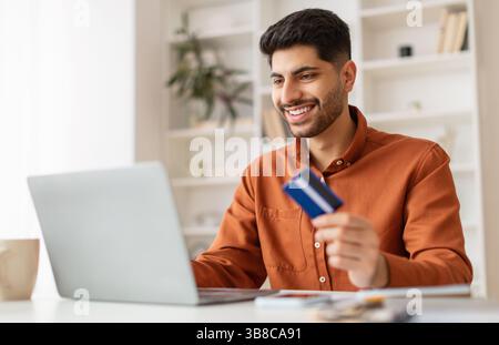 Smiling young man using pc and credit card at home Stock Photo