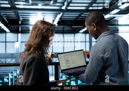 Programmers using laptop in data center, managing server virtualization, running scripts. IT experts using programming language on notebook in server hub, finetuning network protocols Stock Photo