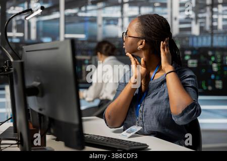 Fatigued data center technician stretching neck while inspecting gear, doing maintenance tasks. Exhausted server farm employee relaxing tensed muscle joints taking break from conducting system checks Stock Photo