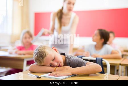 Tired school boy sleeping in classroom during lesson Stock Photo