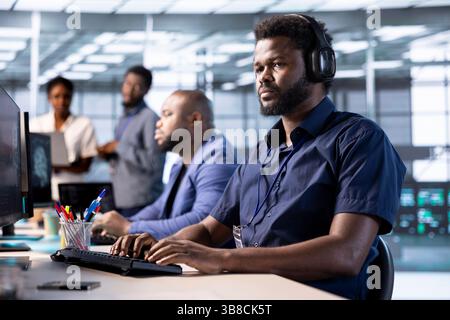 Cybersecurity expert wearing headphones, listening music while monitoring security incidents affecting server hub network. Developer hearing songs in data center and protecting company from threats Stock Photo