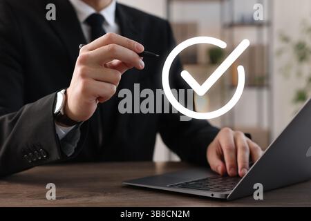 Approved. Man using laptop and touching virtual screen with check mark at table, closeup Stock Photo