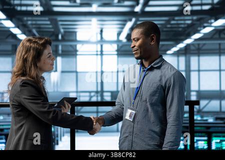 Data center system administrators meeting with inspector arriving in workplace to review equipment. IT specialist doing handshake with supervisor overseeing server farm infrastructure Stock Photo