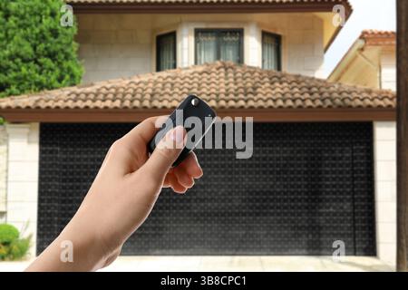 Woman using remote to control garage door outdoors, closeup Stock Photo
