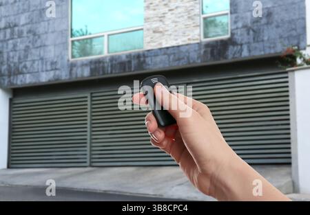 Woman using remote to control roller shutters outdoors, closeup Stock Photo