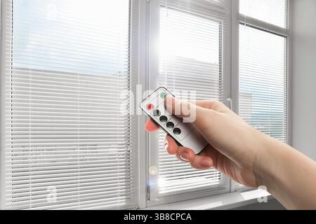 Woman using remote to control blinds in room, closeup Stock Photo