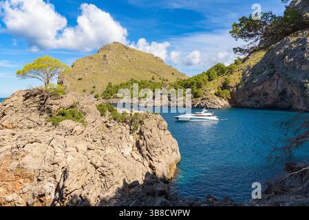 luxurious yacht rests peacefully in the crystal-clear blue waters of Cala de Sa Calobra, surrounded by dramatic cliffs and lush greenery on the island Stock Photo