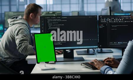 Green screen table in data center in front of IT support specialists working together, supervising server rows. Employees overseeing supercomputers using mockup device, camera A Stock Photo