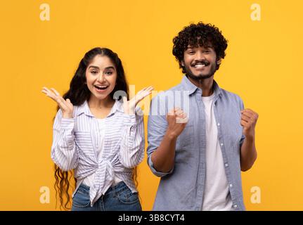 Wow. Overjoyed indian spouses gesturing in amazement looking at camera over yellow studio background Stock Photo