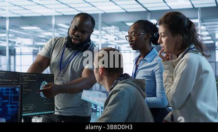 Technician doing brainstorming with colleagues to fix error in code affecting server room AI workloads. Team of artificial intelligence engineers repairing data center systems together, camera A Stock Photo