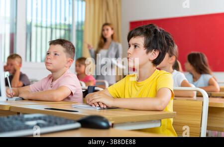 Tween boy listening to schoolteacher and writing in notebook in class Stock Photo