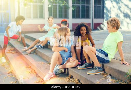 Positive tweenagers friendly blabbing while sitting on steps outdoors Stock Photo