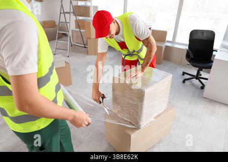 Male loaders wrapping boxes with stretch film in warehouse Stock Photo