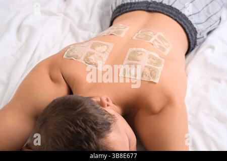 Sick young man with mustard plasters lying on bed, closeup Stock Photo
