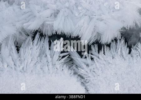 Delicate frost crystals cover a dark surface, showcasing nature's artistry in winter. The intricate designs reflect the cold atmosphere and beauty of Stock Photo
