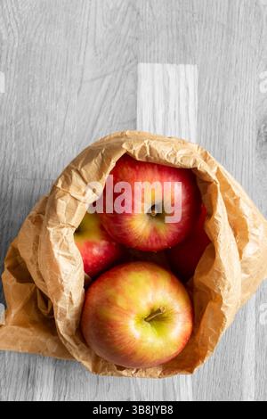 Apples in a brown paper bag on a wood background with selective colour.  Environmentally friendly packaging concept Stock Photo