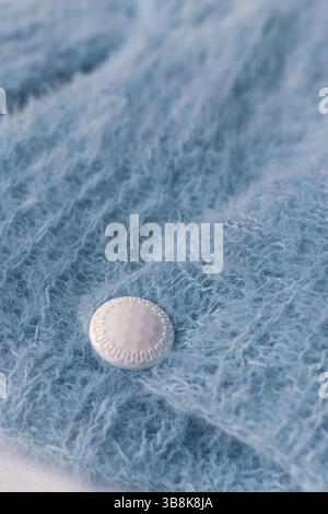 Blue knitted cardigan with white button on white background. Soft blue knitted sweater in details. Knitting pattern background. Summer knitted fashion Stock Photo