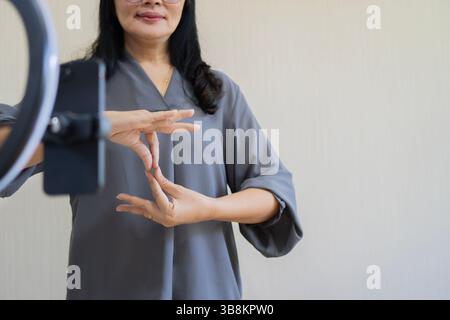 Happy mature Asian woman with disability using cell phone for broadcasting with copy space. Sign language concept. Stock Photo