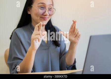 Smiling friendly woman in glasses with laptop and talking on video call, using sign language, speaking to patient with hearing disability Stock Photo
