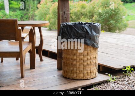 Black plastic garbage bag in a bamboo basket bin in a local natural cafe. Trash Bamboo Basket. Pollution concept. Stock Photo