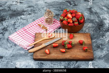 High angle view a glass jar and cinnamon on red gingham tablecloth with kitchen utensils and a bowl of strawberries on dark blue marble background. ho Stock Photo