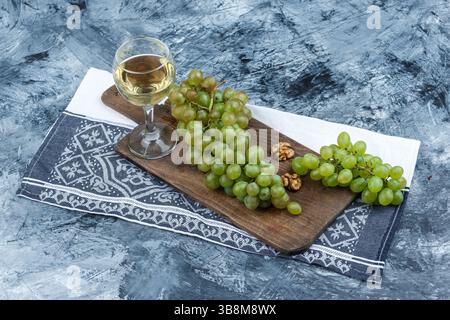 white grapes, walnuts on a cutting board with kitchen towel, glass of whisky high angle view on a dark blue marble background Stock Photo