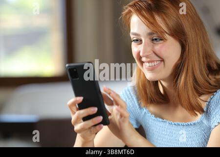 Happy woman browsing phone smiling at home Stock Photo