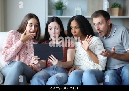 Surprised group of friends checking tablet content sitting on a couch at home Stock Photo