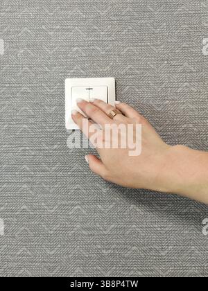 Turning light on / off. Woman pressing light switch on patterned wall, close-up Stock Photo