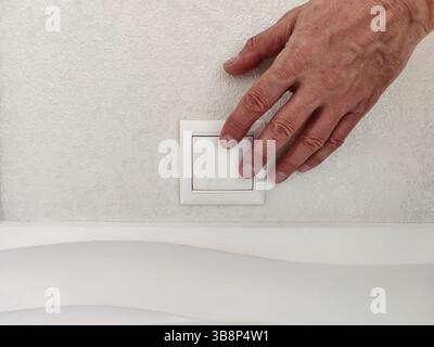 Turning light on / off. Man pressing light switch on white wall, close-up Stock Photo