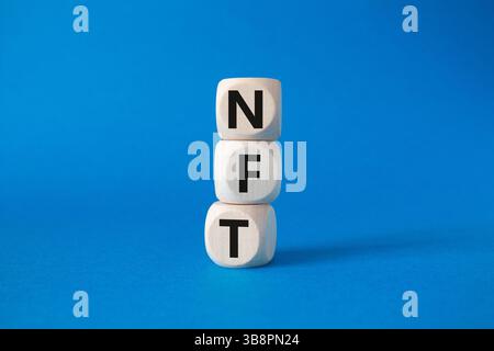 NFT - non-fungible token symbol. Concept word NFT on wooden cubes. Beautiful blue background. Business and NFT concept. Copy space. Stock Photo